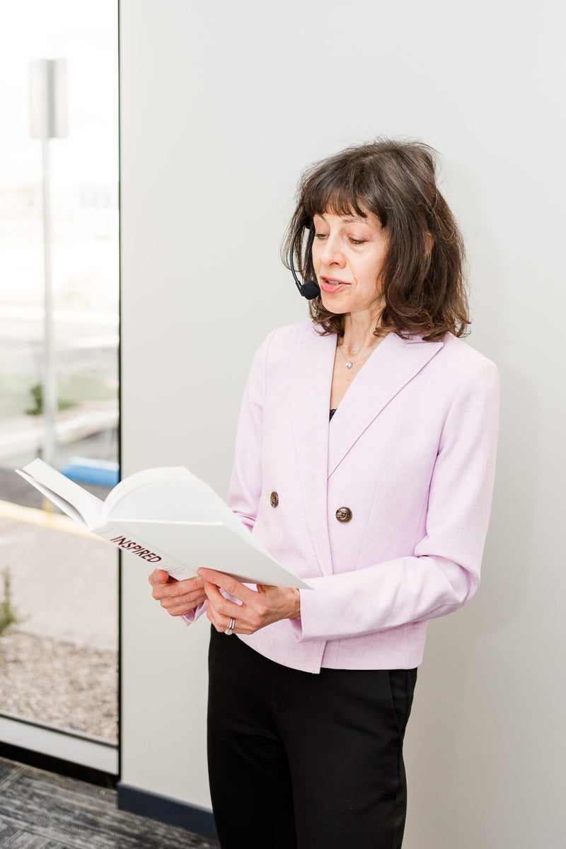 Middle-aged white woman in a pink blazer reading a book