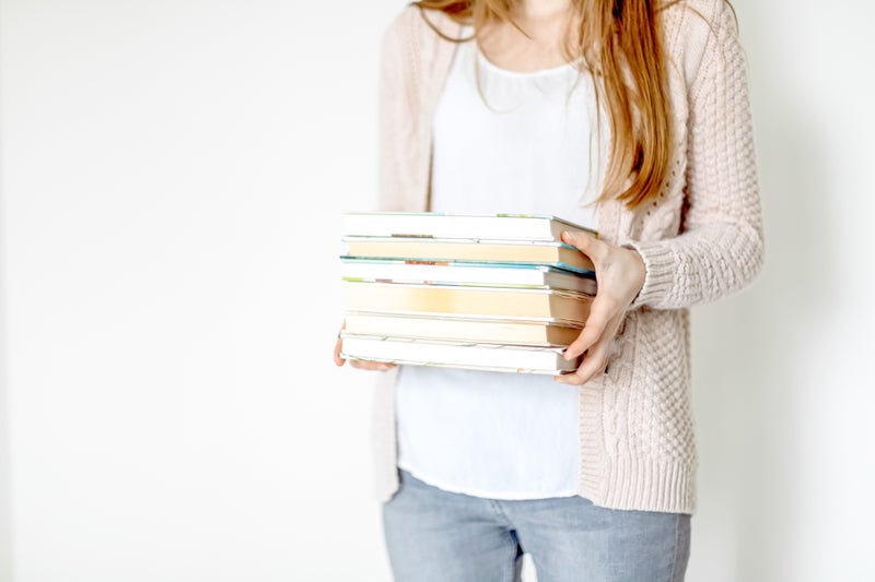 Close up of a white woman's hands holding a stack of six textbooks